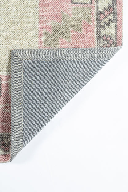 Colorful woven rug with pink and beige pattern; folded corner reveals blue denim-like underside.