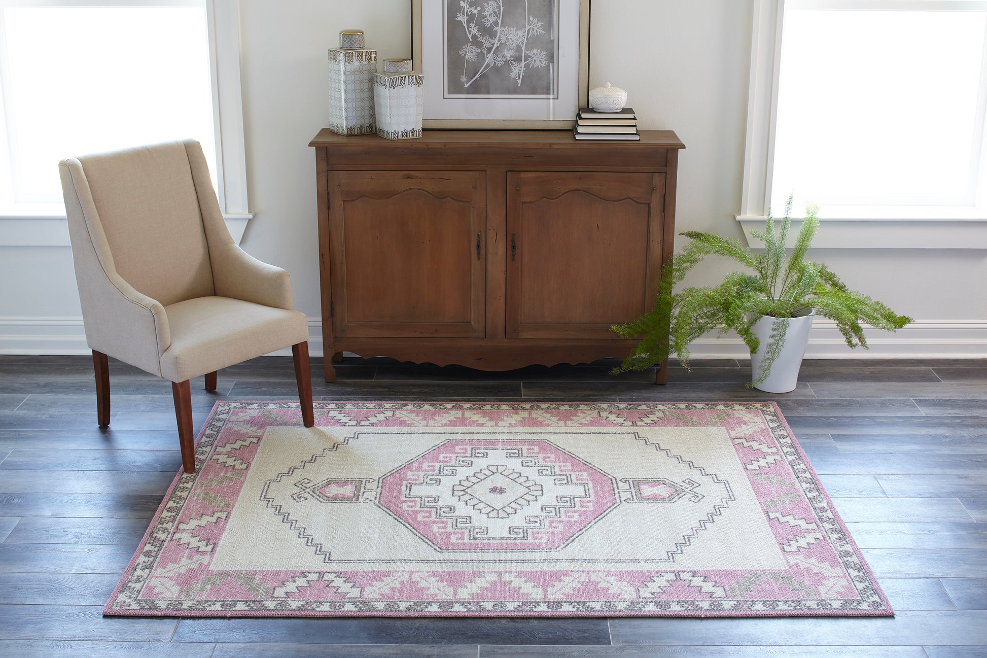 Pink geometric rug 2' x 3' in a bright living room, with a traditional wooden sideboard, beige upholstered armchair, and a potted fern.