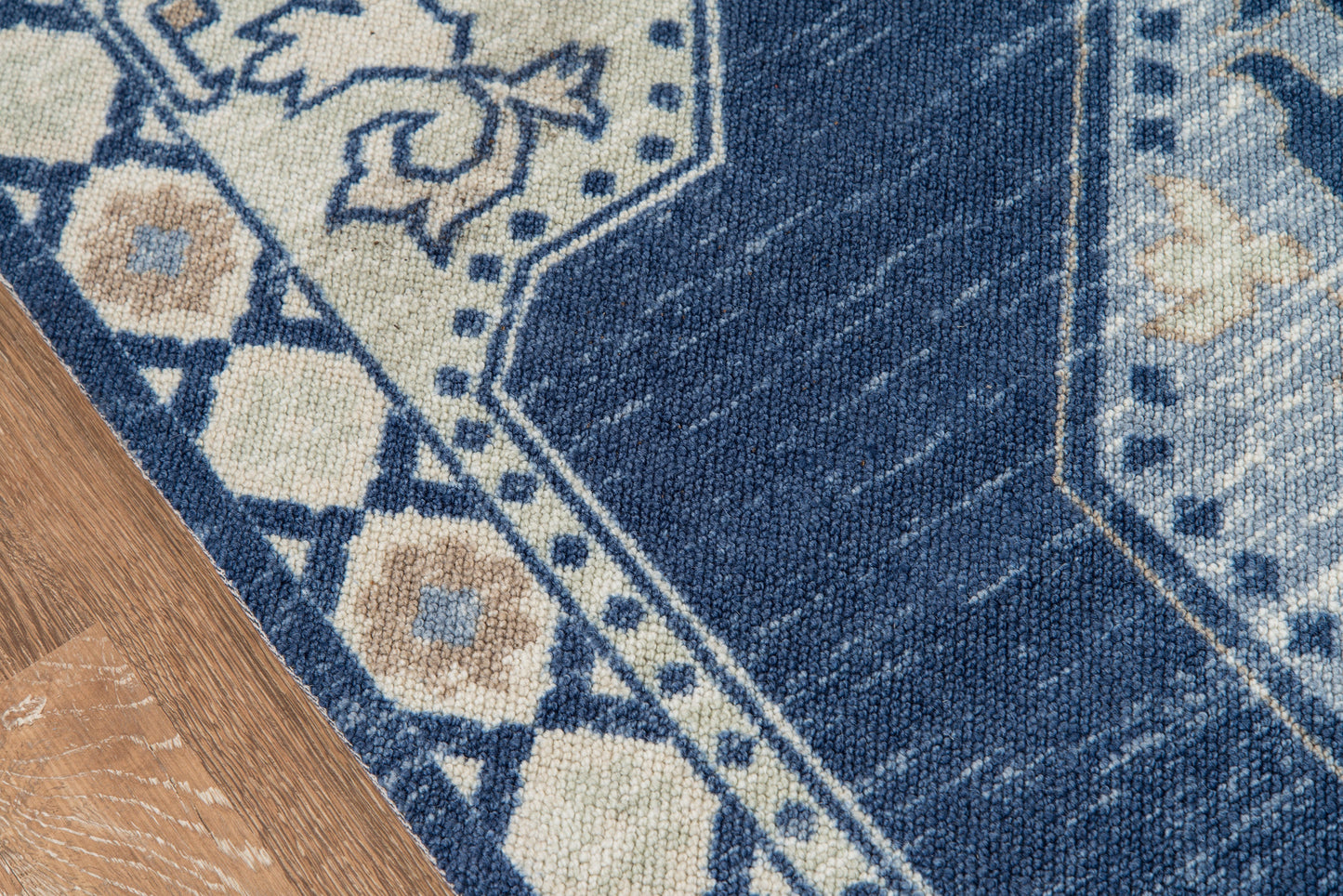 Blue oriental rug with ivory floral motifs and geometric border, partly on a wooden floor.