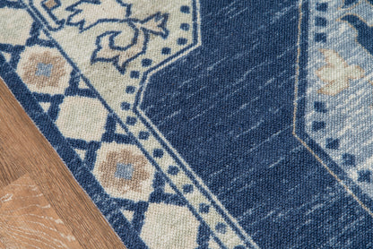 Blue oriental rug with ivory floral motifs and geometric border, partly on a wooden floor.