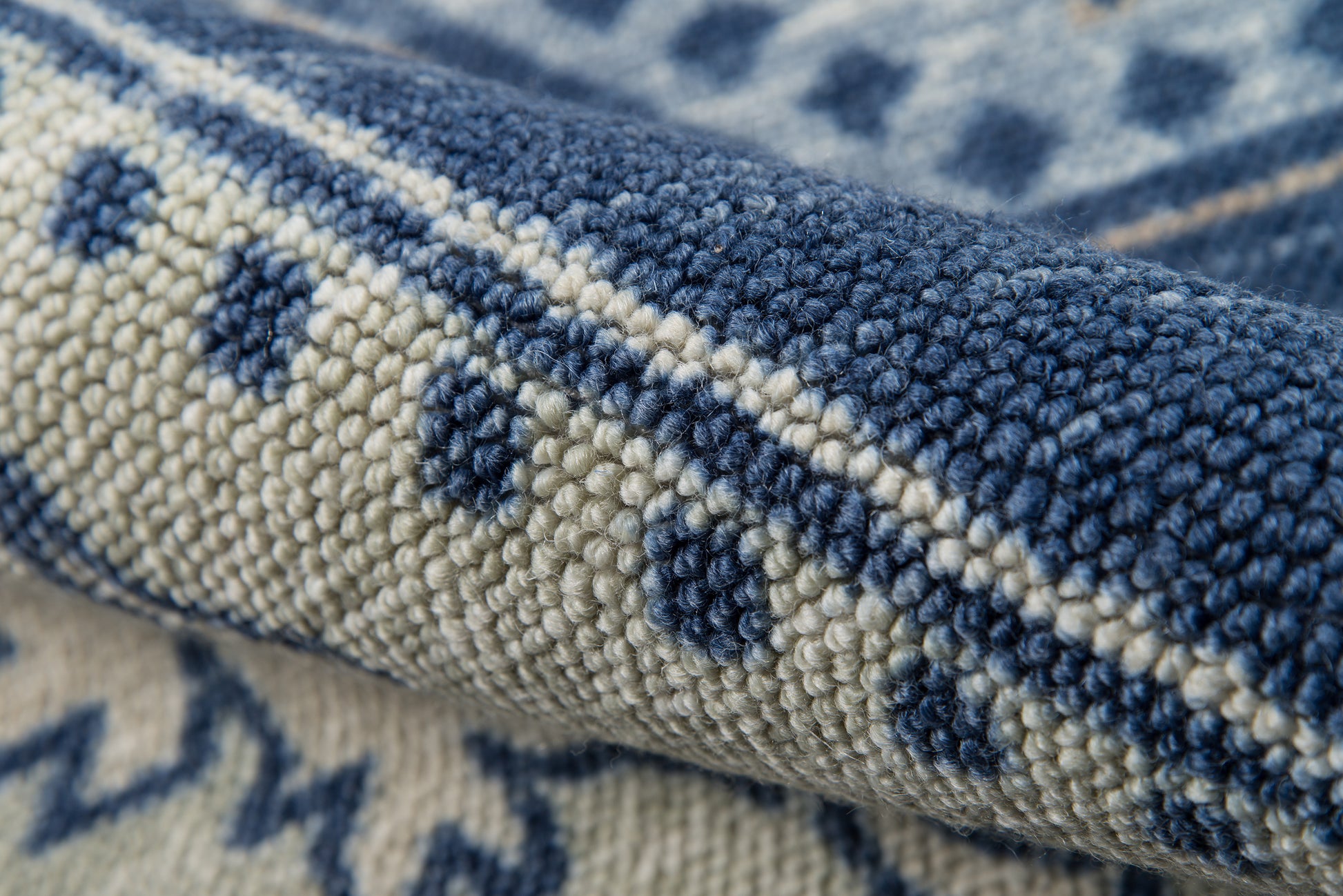 Close-up of a blue and ivory woven rug with dotted geometric pattern, thick looped texture and rolled edge.