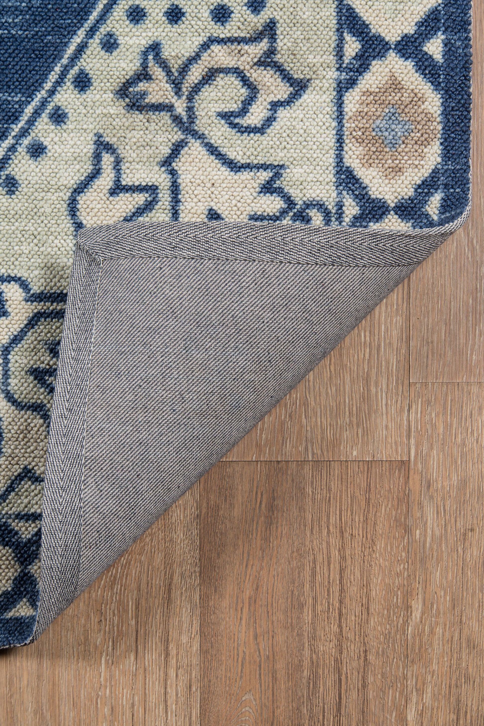 Navy and ivory woven rug with floral motifs; folded corner reveals gray backing on wood floor.
