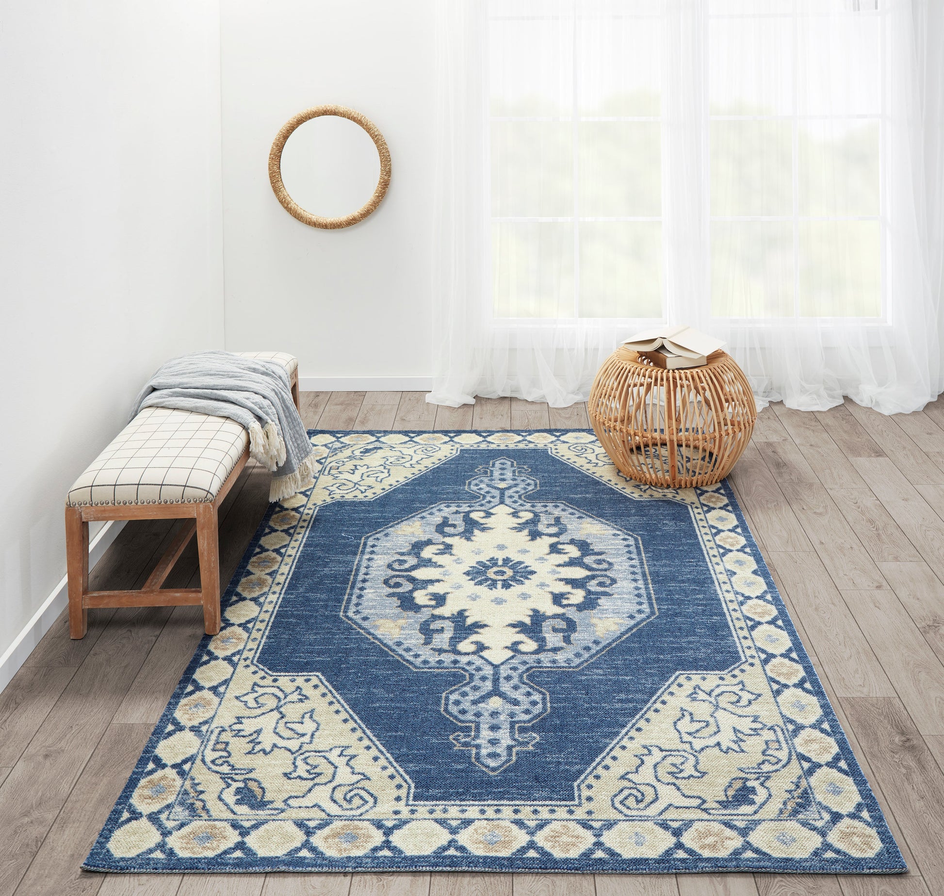 Blue and ivory oriental rug with geometric medallion, paired with a wooden bench, plaid cushion, and round wicker wall decor.