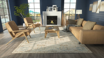 Modern living room with blue walls, tan leather chairs, beige sofa, wooden coffee table, fireplace, plant, and patterned rug.