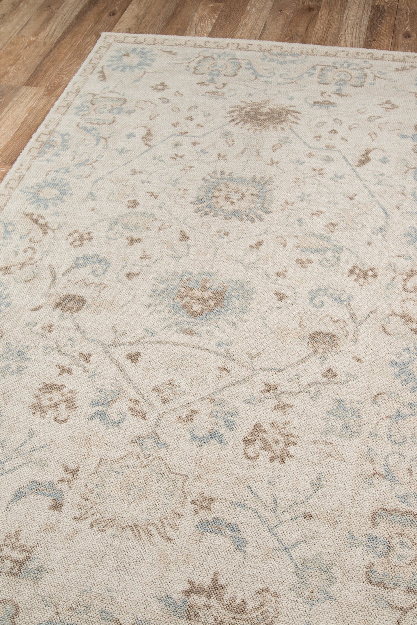 Rectangular beige oriental area rug with pale blue and taupe floral motifs on a wooden floor.