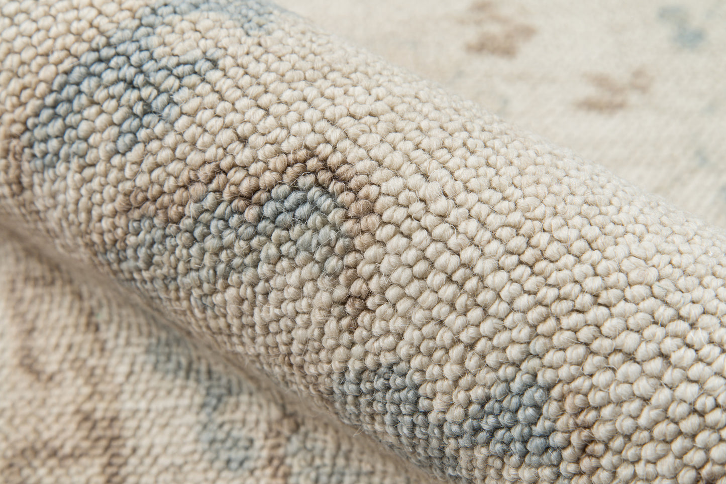 Close-up of beige loop-pile rug showing pale blue-gray pattern and soft textured weave.