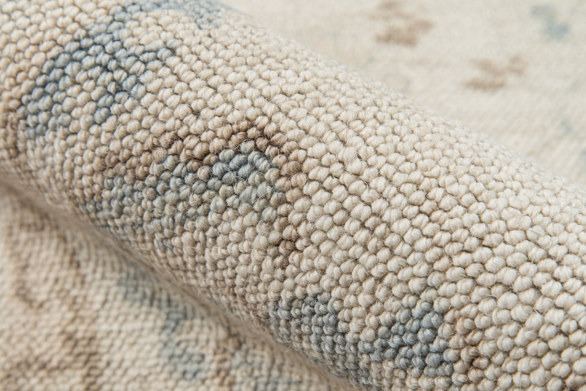 Close-up of beige loop-pile rug showing pale blue-gray pattern and soft textured weave.
