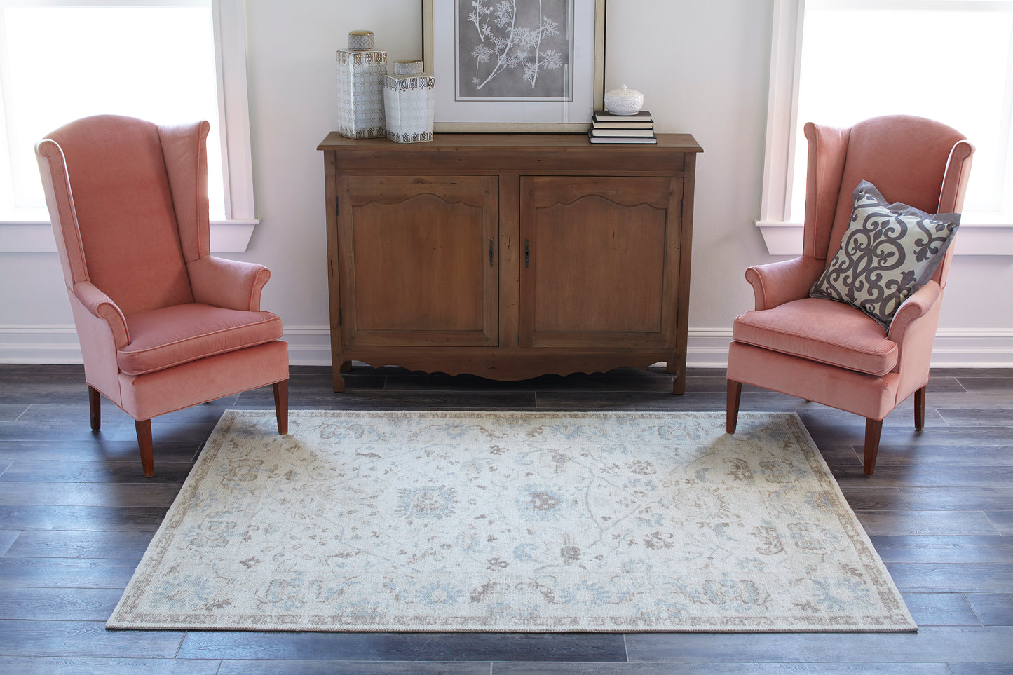 Two coral pink upholstered armchairs with curved backs flank a wooden sideboard on a light patterned area rug.