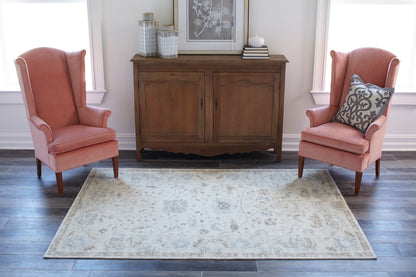 Two coral pink wingback chairs flank a brown wooden sideboard topped with vases and art on a light patterned rug.