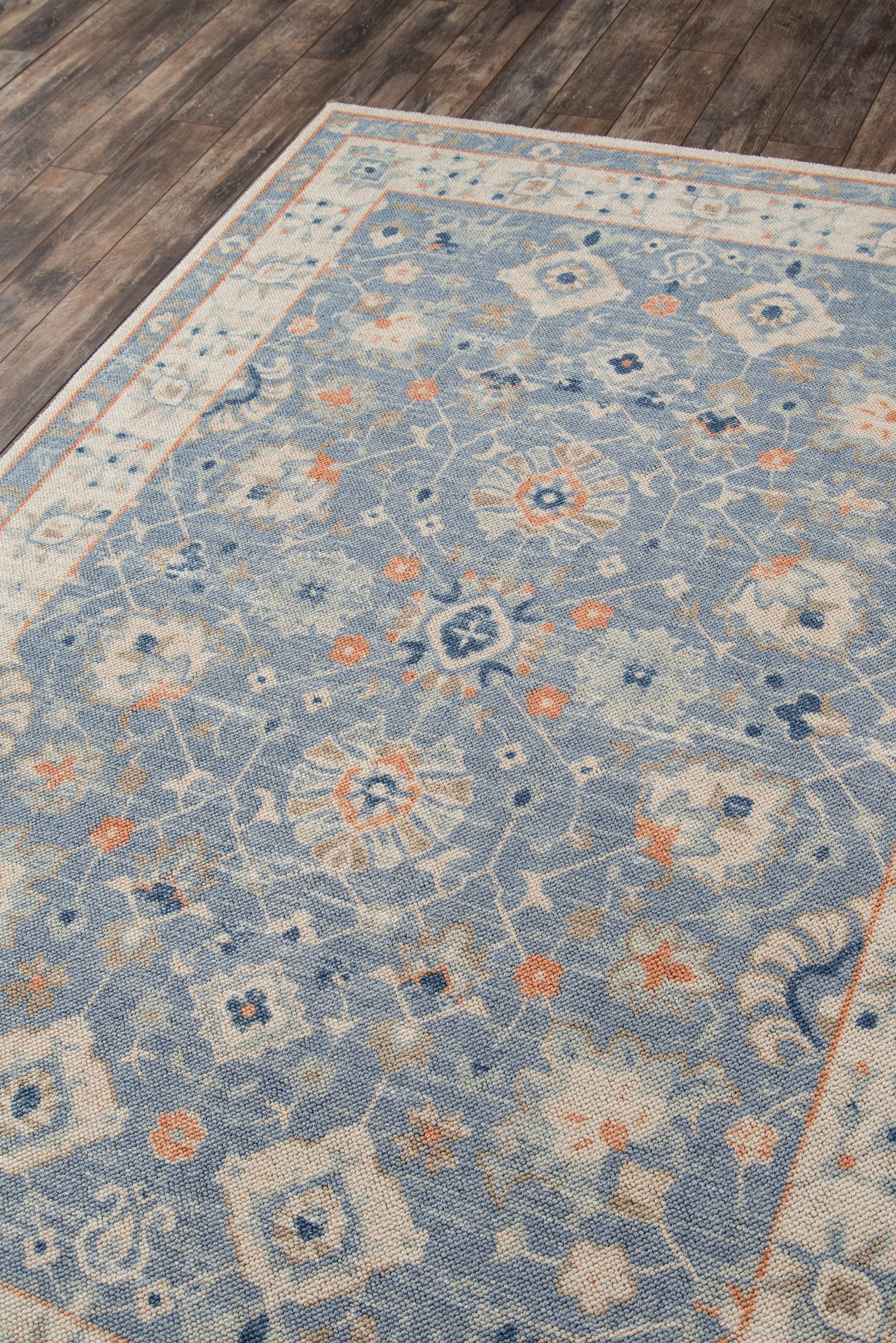 Rectangular blue rug with ivory floral medallions and subtle orange accents on a dark wood floor.
