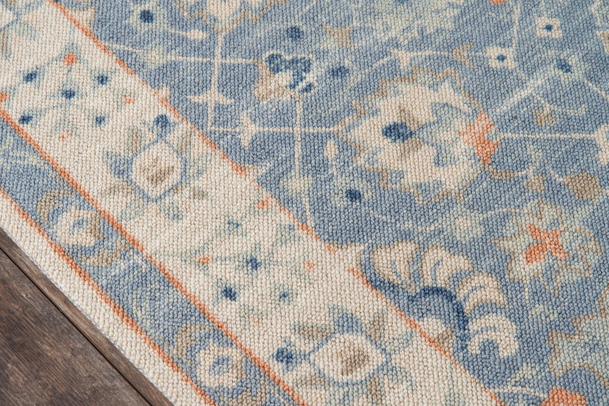 Blue and ivory ornate area rug with orange border in traditional oriental pattern, partially on a wooden floor.