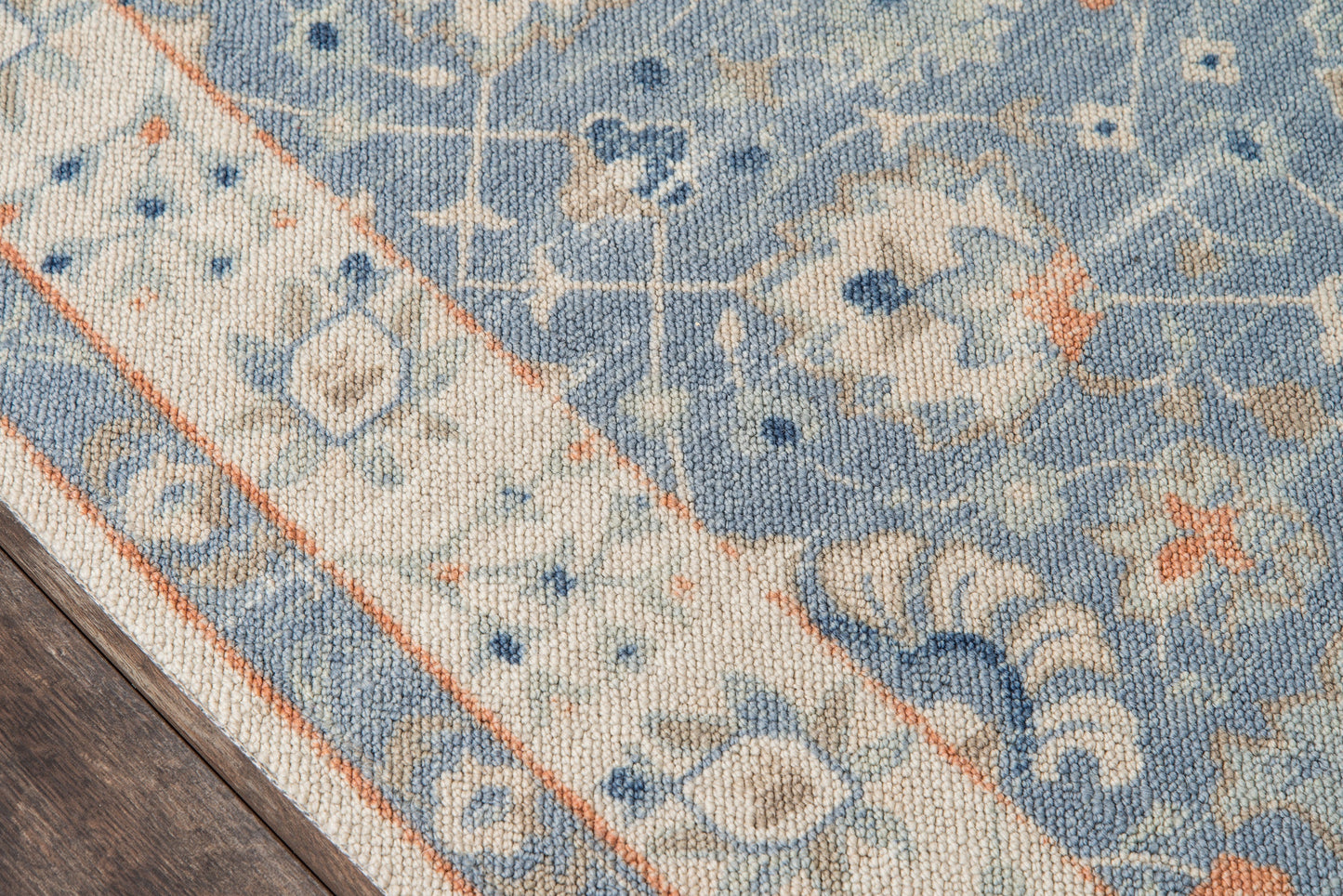 Blue and beige oriental-style area rug with orange border, woven texture and floral motifs on a wooden floor.