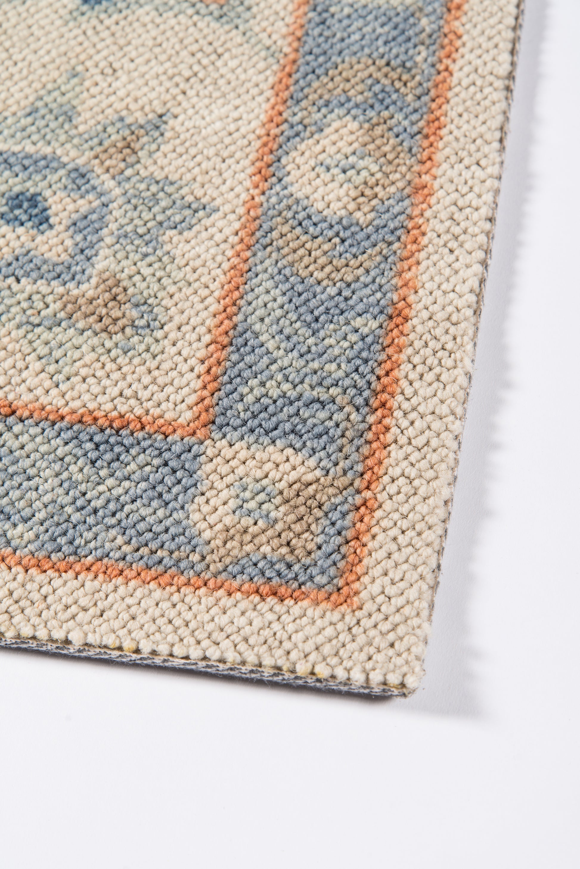 Close-up of a blue and beige patterned rug with an orange border and woven texture.