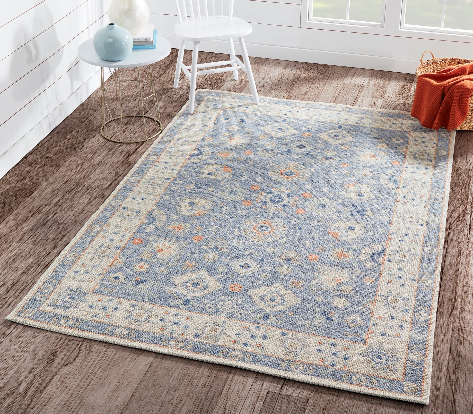 Rectangular blue area rug with ivory border and oriental floral motifs in cream and orange, on wooden floor.