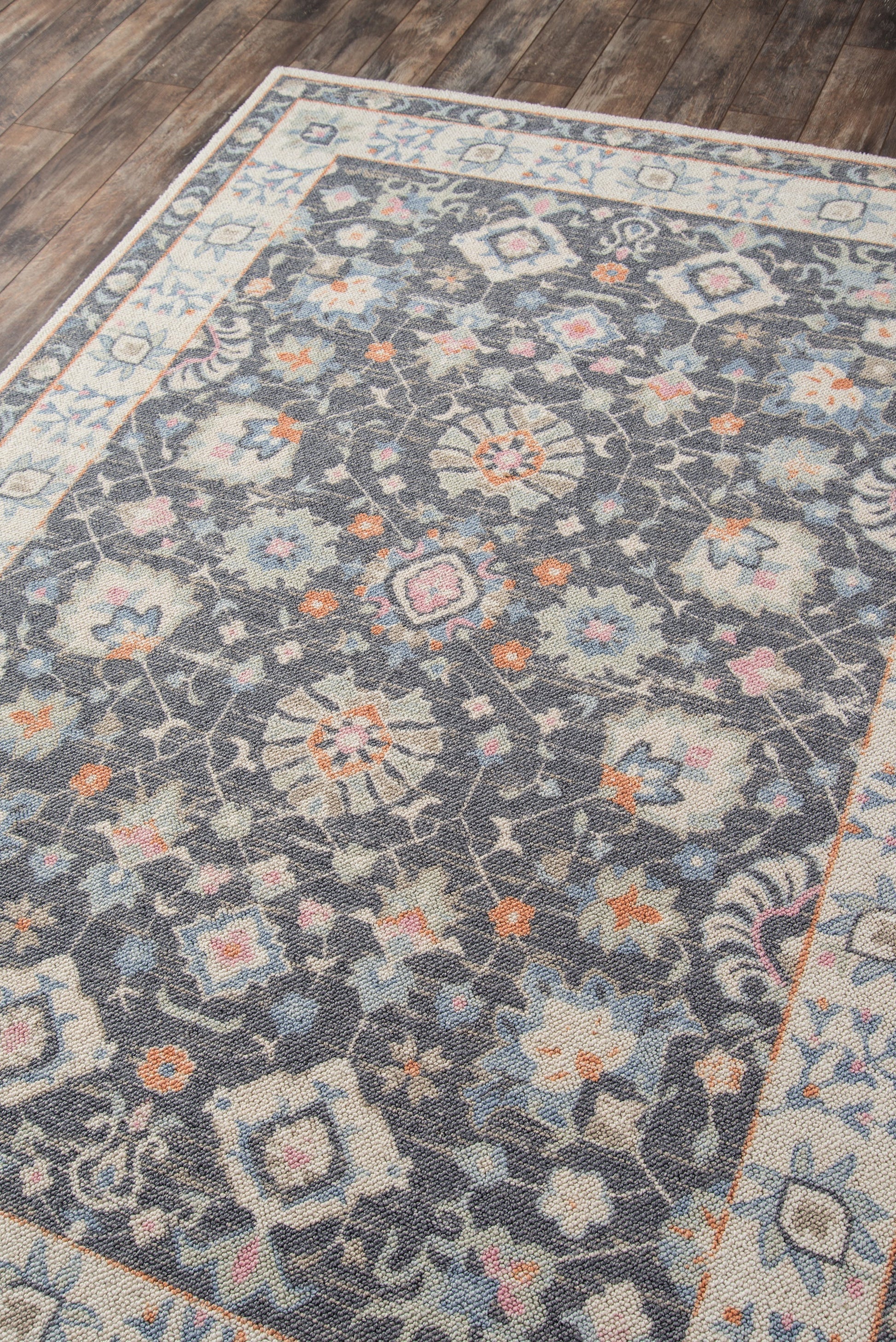 Rectangular area rug with dark blue-gray field, multicolored floral medallions, and light cream border, on wood floor.