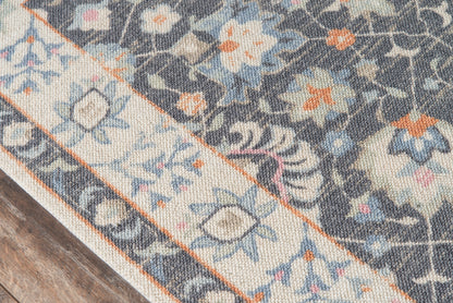 Blue-gray oriental rug with ivory border and floral motifs in orange, blue, and cream; rolled corner on a wooden floor.
