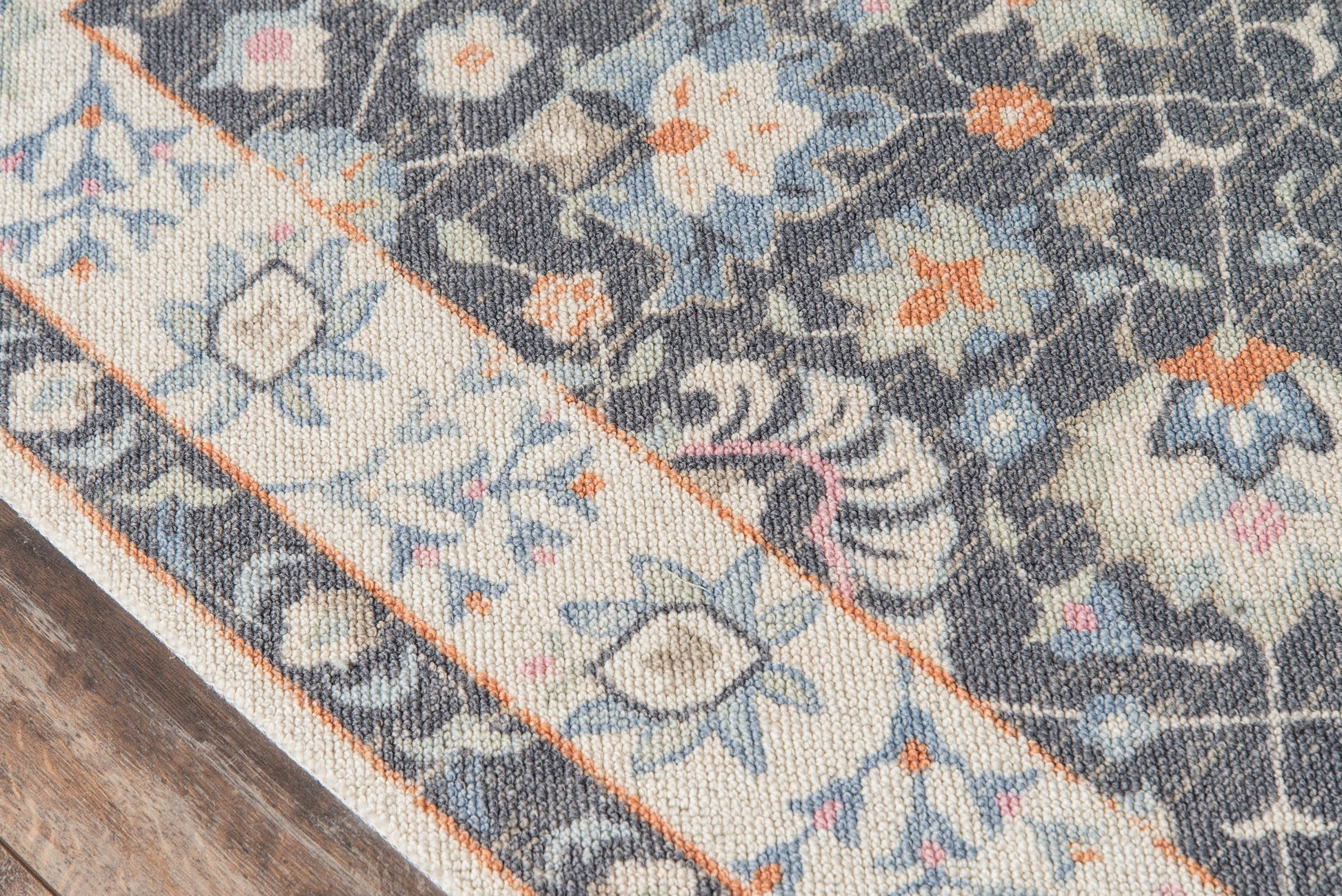 Anatolian-style woven rug with blue, ivory, and orange floral motifs and a bordered edge on a wooden floor.