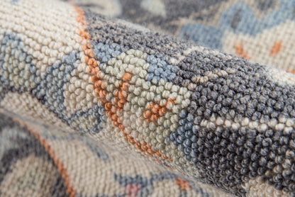 Close-up of a woven wool rug with blue-gray, beige, and orange geometric pattern; plush loop pile, boho-style.