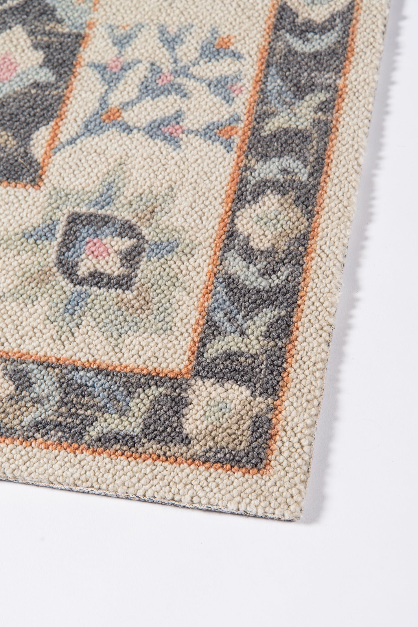 Close-up of a traditional patterned rug edge: cream/beige field, orange border, blue-gray floral motifs.