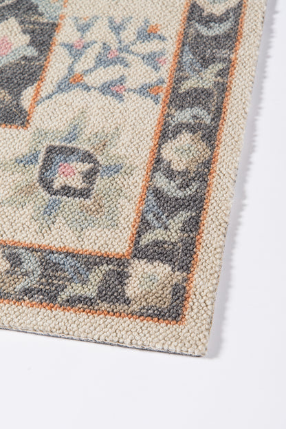 Close-up of a traditional patterned rug edge: cream/beige field, orange border, blue-gray floral motifs.