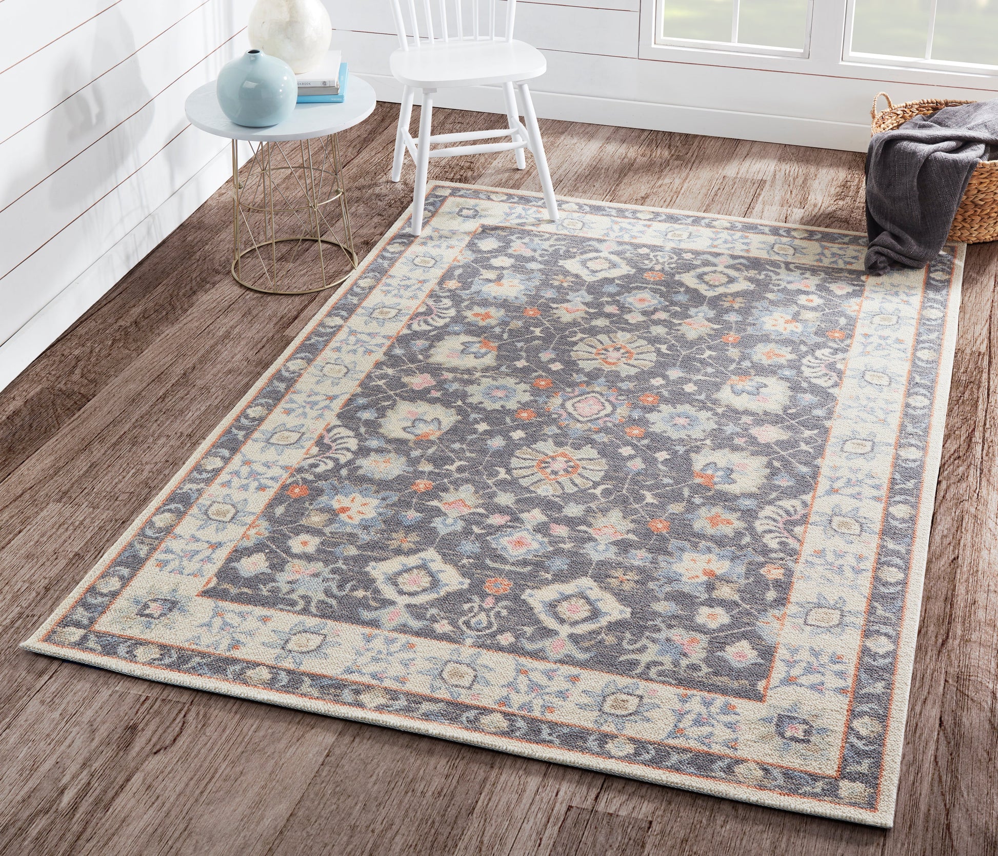 Ornate blue-gray area rug with ivory and rust accents, floral medallion center and decorative border on a wooden floor.