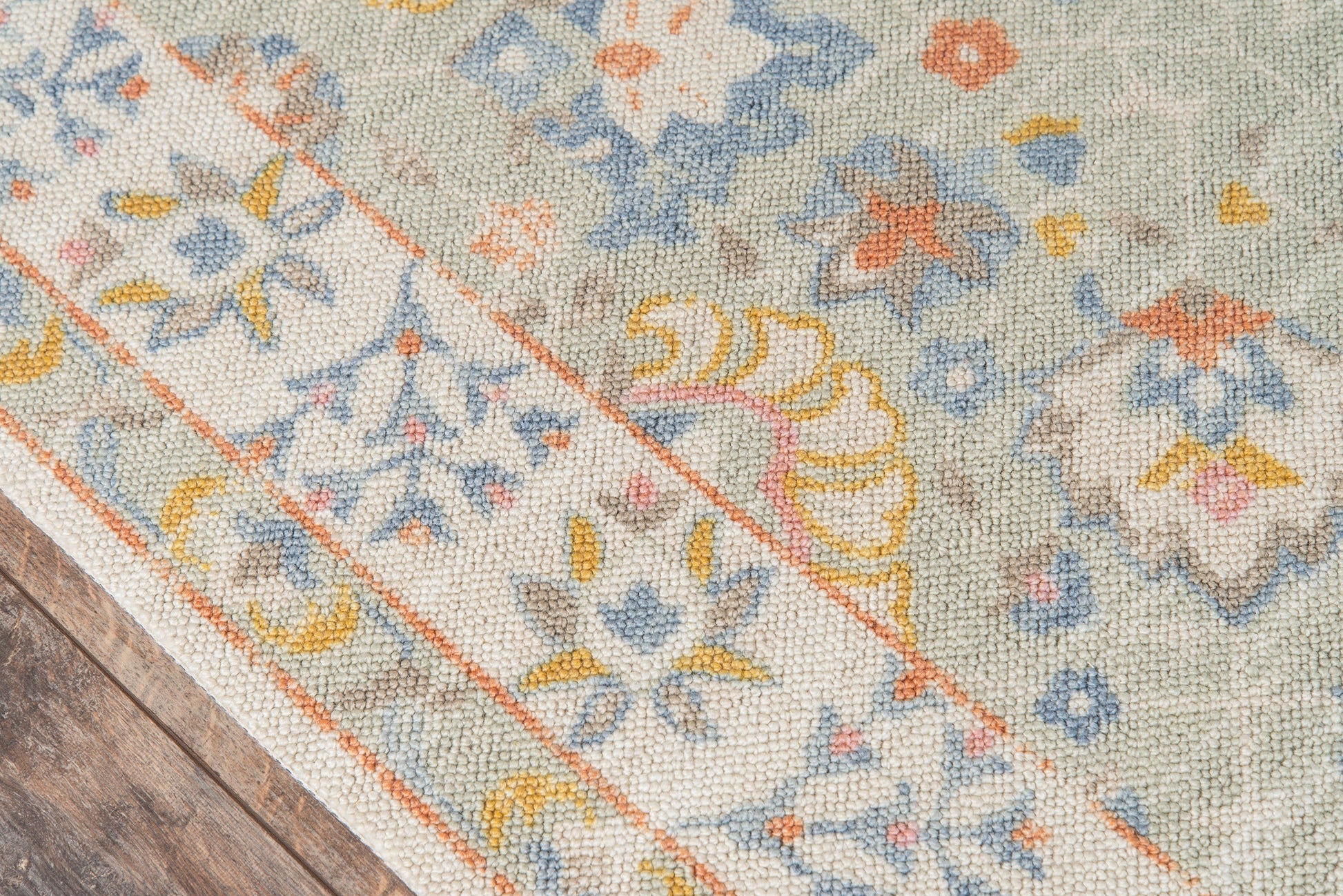 Pastel floral woven rug with ivory background, blue, yellow and orange motifs, bordered edge on wooden floor.