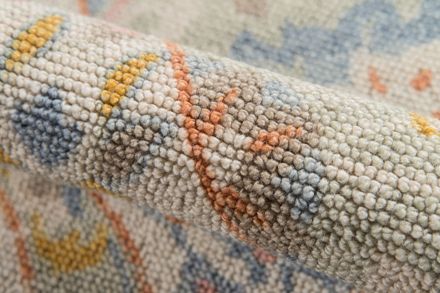 Close-up of a textured woven rug with beige/gray pile and blue, yellow & orange geometric motifs.