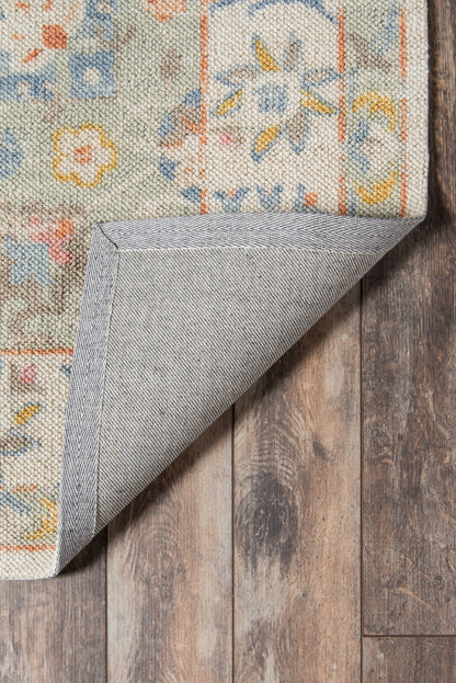 Pastel floral woven rug with blue, orange and yellow hues; folded corner reveals gray backing on a wooden floor.