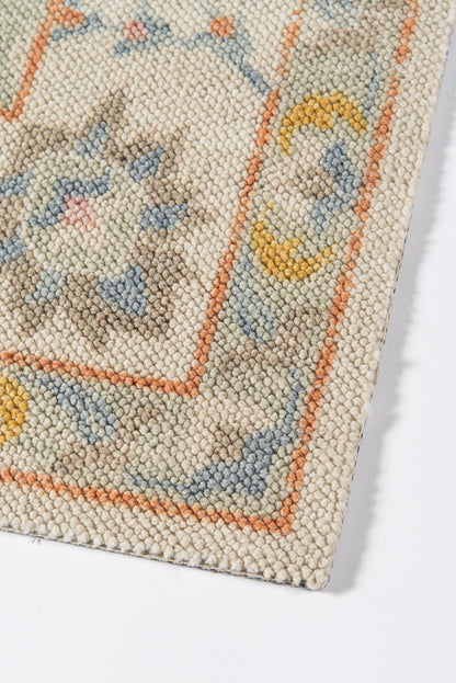 Close-up of a cream woven rug with orange borders, blue floral motifs and pale yellow circular accents; vintage oriental style.