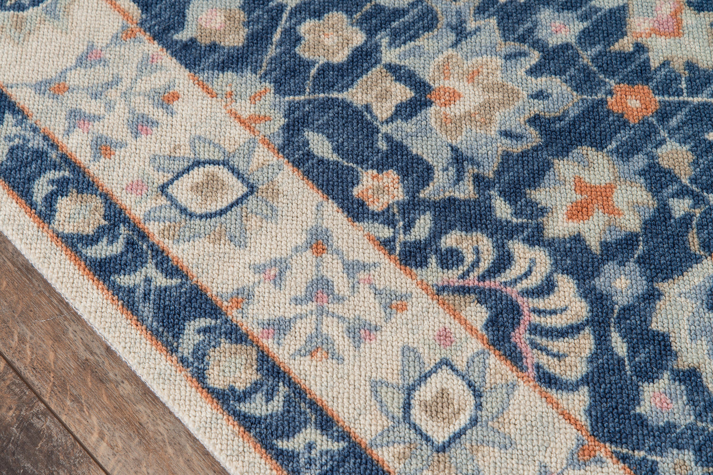 Navy blue floral area rug with cream border and orange accents on wooden floor.