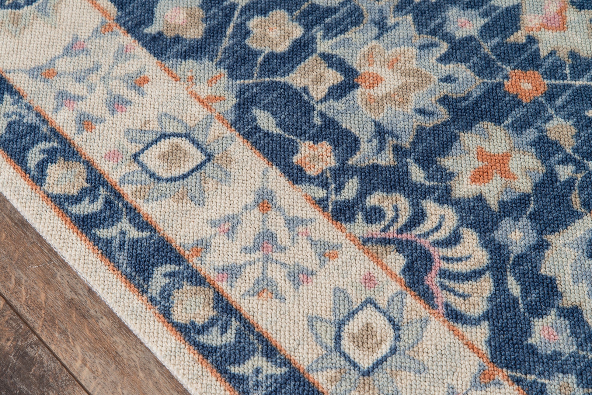 Woven area rug with blue and ivory floral pattern, beige border, on wooden floor.