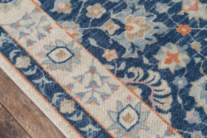 Woven area rug with blue and ivory floral pattern, beige border, on wooden floor.