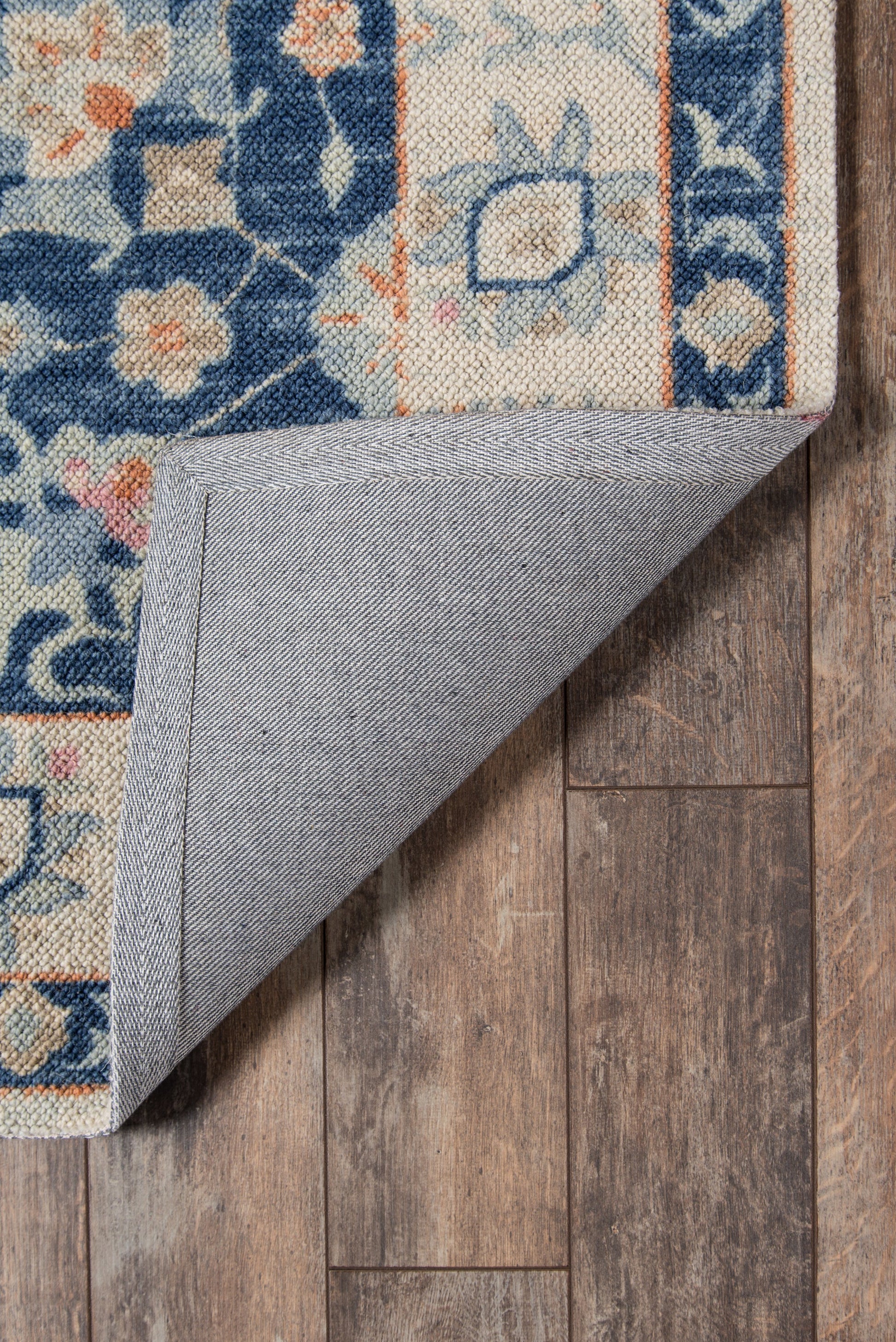 Blue and ivory floral Persian-style rug, folded corner reveals gray backing on wooden floor.
