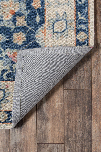 Blue and cream floral area rug with orange accents; woven textile, folded corner reveals gray backing on wooden floor.