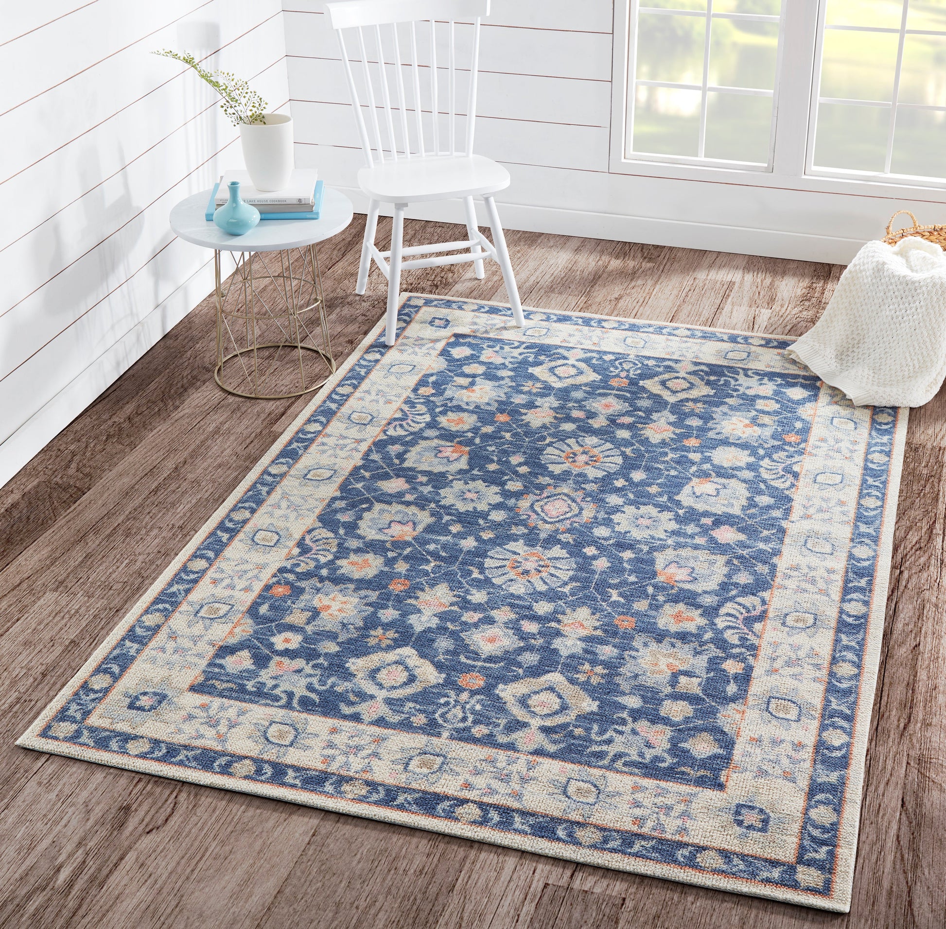 Blue and ivory ornate oriental rug on wood floor; sunlit white room with a white chair and round blue side table.