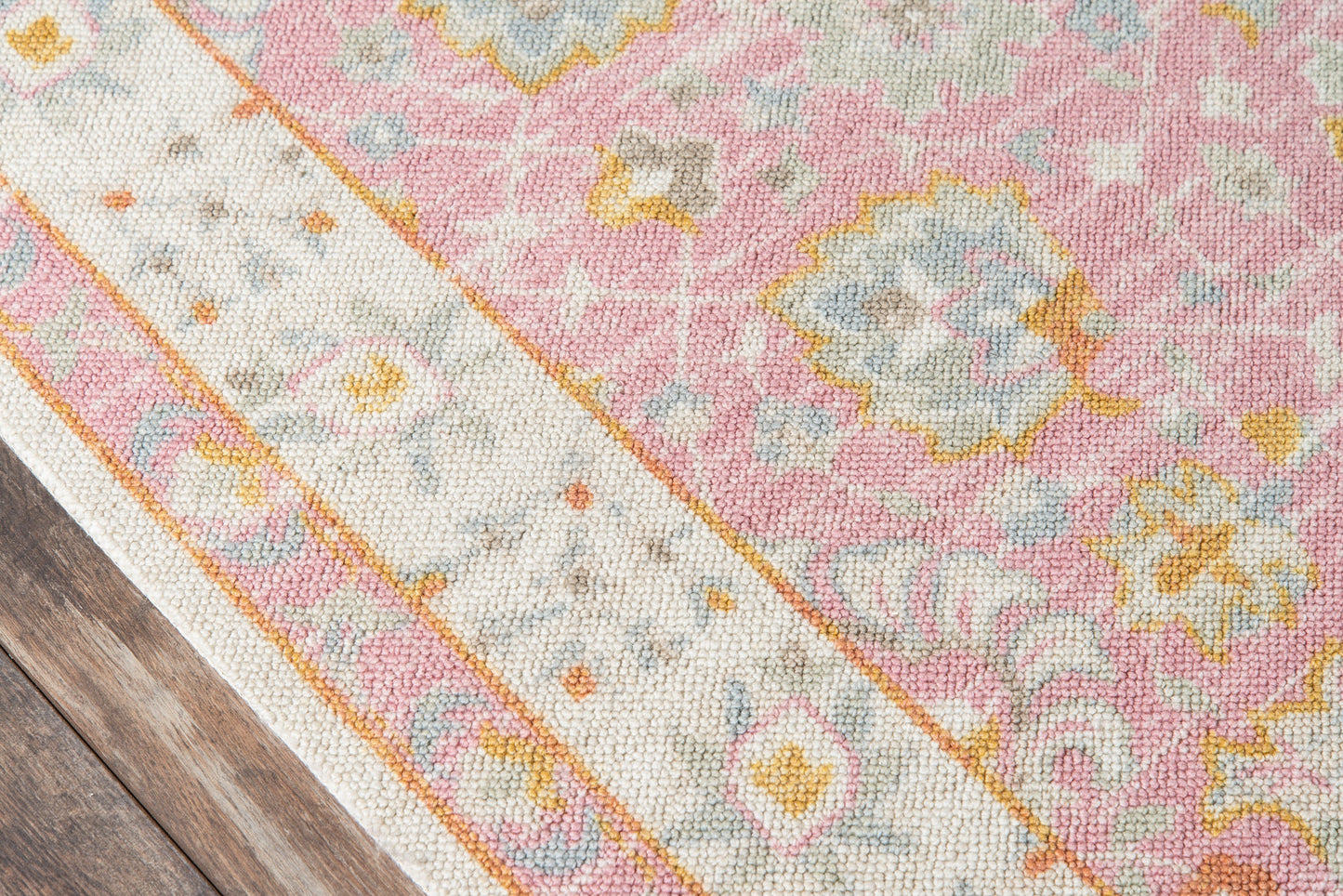 Pastel pink floral area rug with ivory border, blue and yellow accents, on a wooden floor.