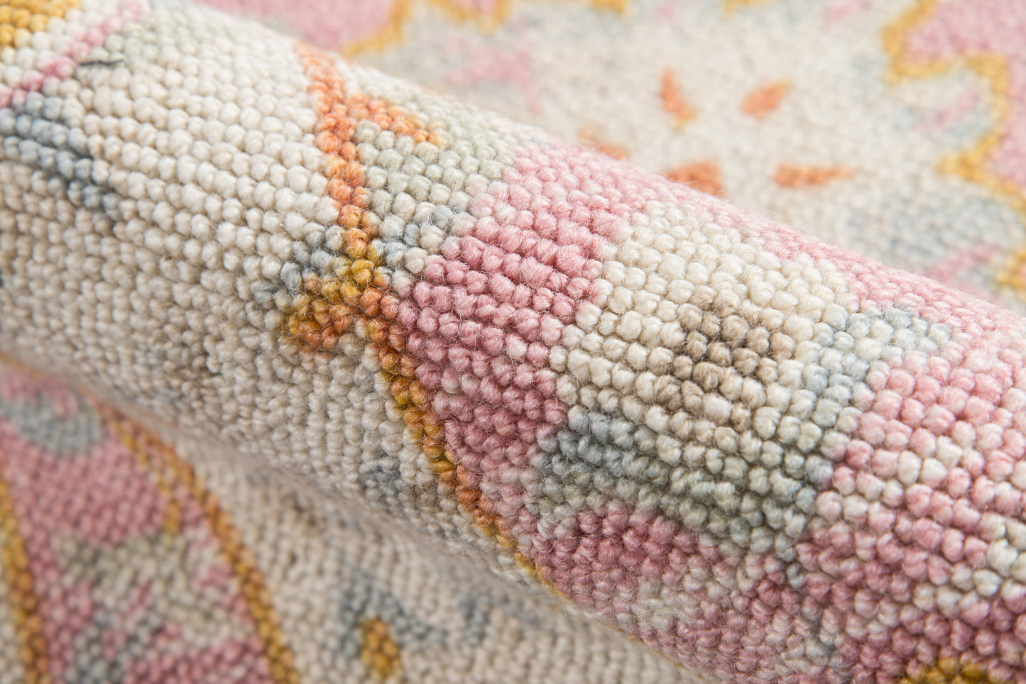 Close-up of a pastel woven rug with looped pile in pink, cream, pale blue and yellow geometric pattern.