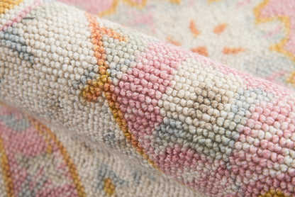 Close-up of a pastel woven rug with looped pile in pink, cream, pale blue and yellow geometric pattern.