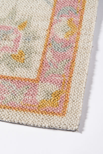 Close-up of a cream hand-knotted rug with pastel pink, peach, yellow border and geometric motif.