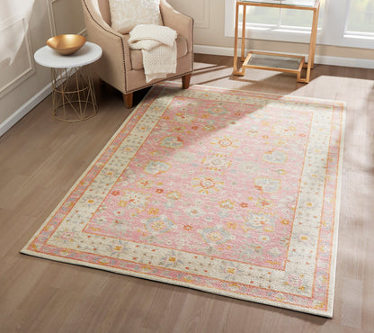 Pastel pink floral rug with pale cream border in a light living room beside a beige armchair and gold side table.