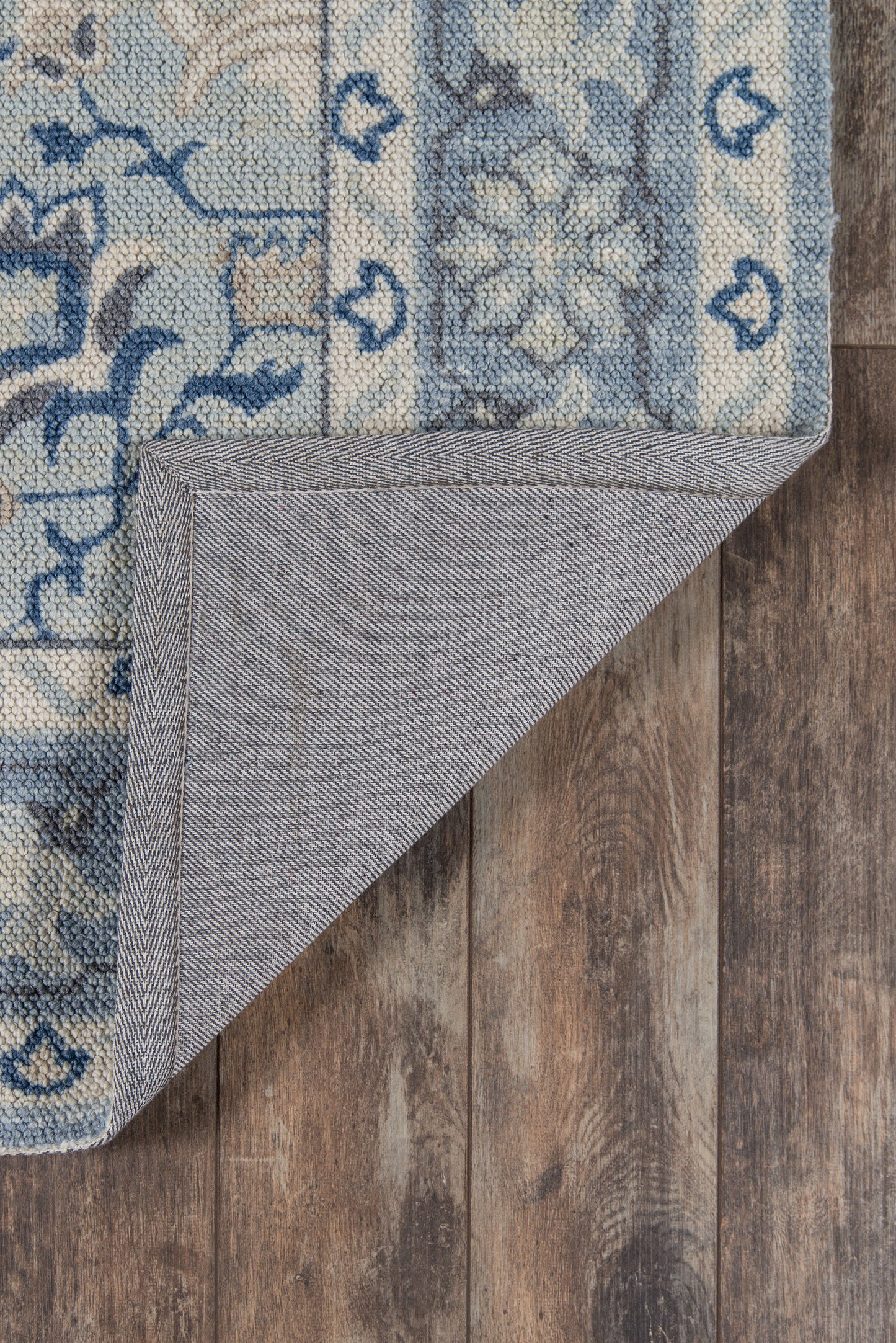 Rectangular blue & ivory oriental-style rug with floral medallions; gray backing visible at folded corner on wooden floor.