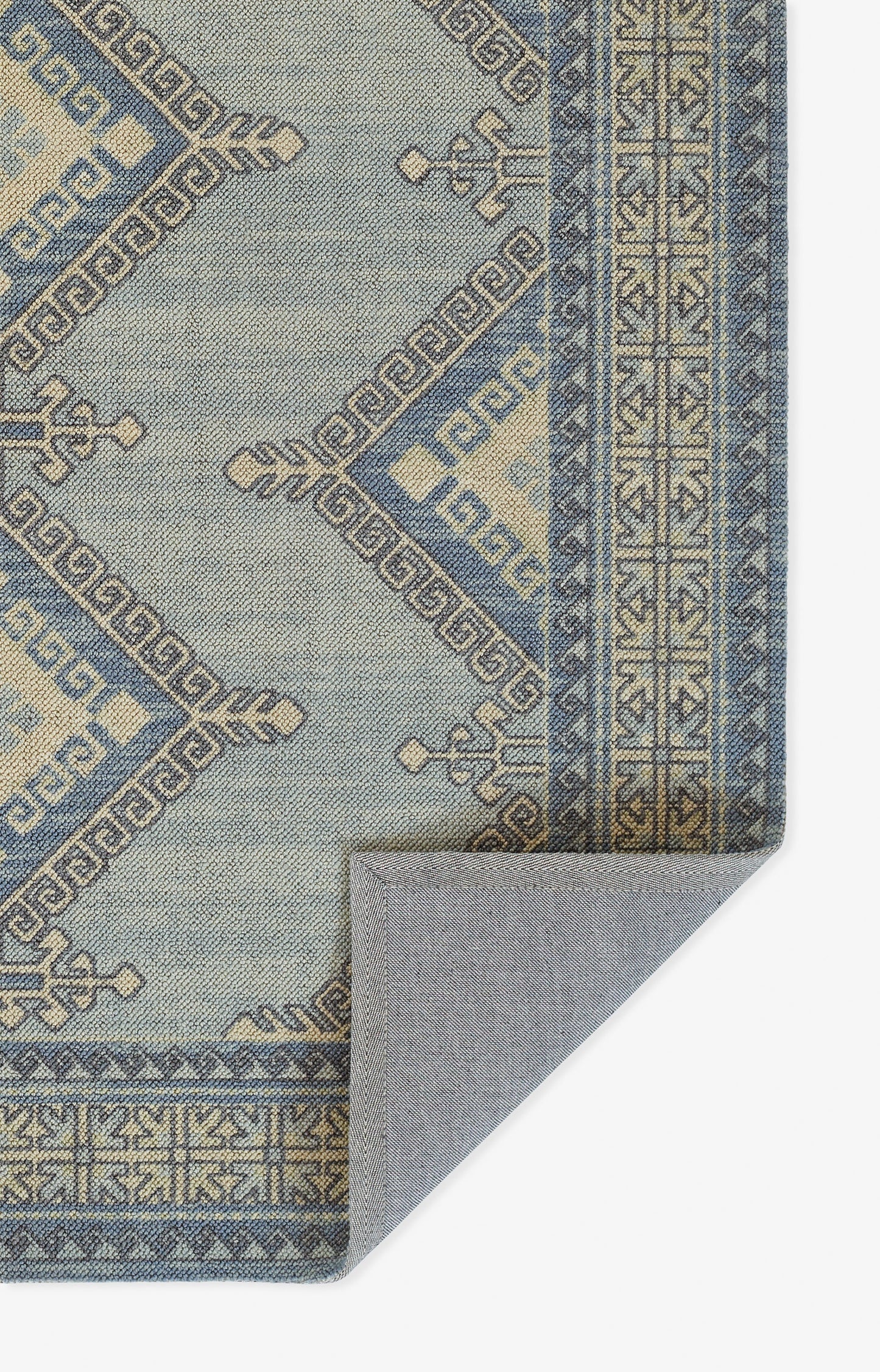 Blue-grey geometric rug with Greek key borders; woven beige motifs on blue, corner folded to show backing.