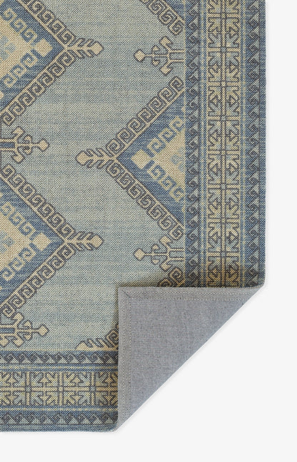 Blue woven rug with geometric Greek-key border and diamond motifs; folded corner reveals light grey underside.