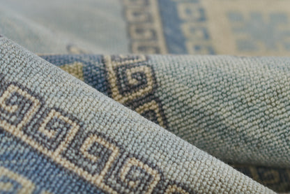 Blue woven rug with beige Greek key border, textured fabric, folded.