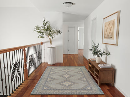 Blue-gray geometric area rug on hardwood floor beside a wooden handrail with iron balusters, tall plant, console table, and framed art.