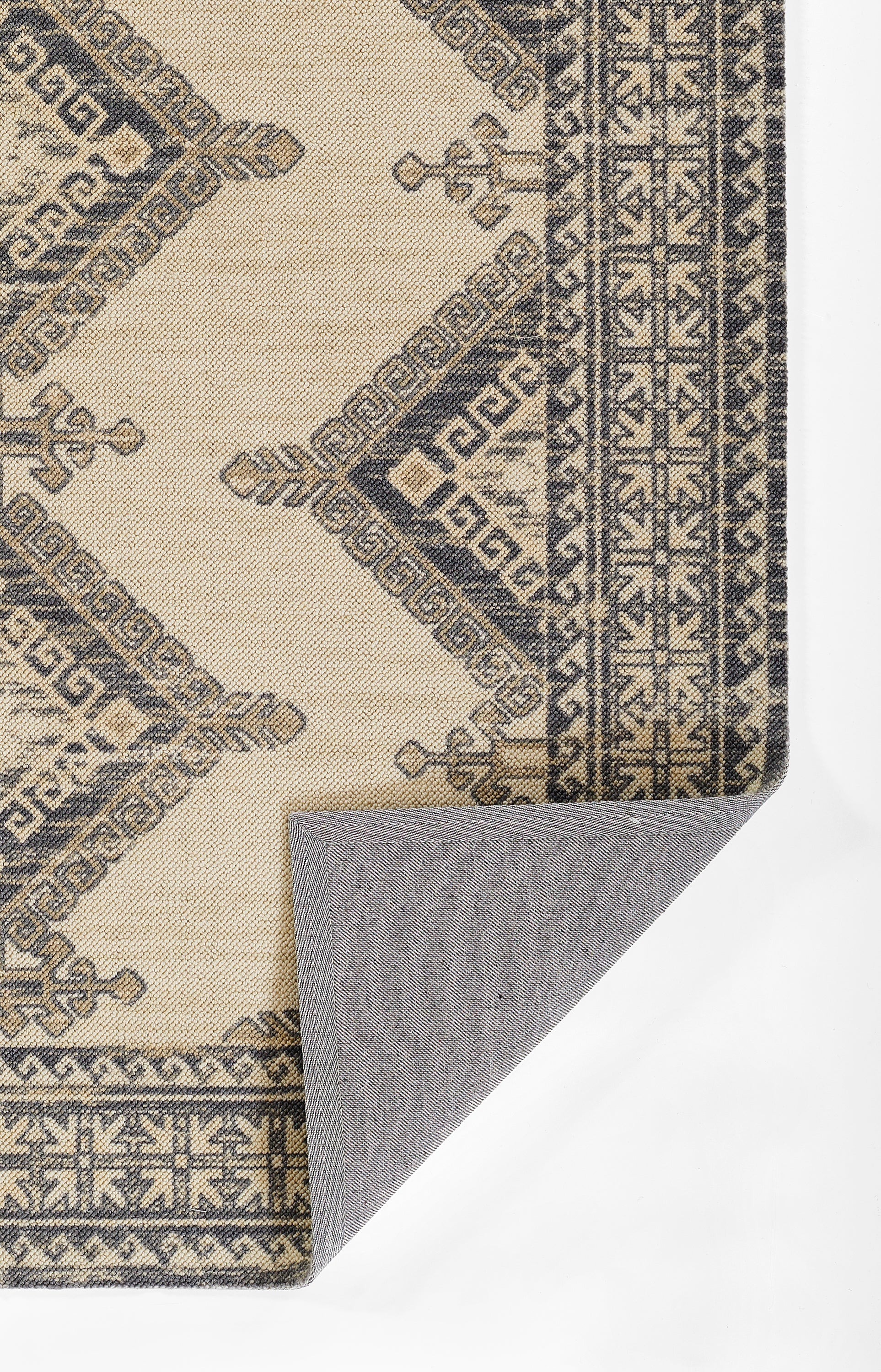Beige oriental area rug with dark blue geometric borders and diamond motifs; folded corner reveals gray backing.