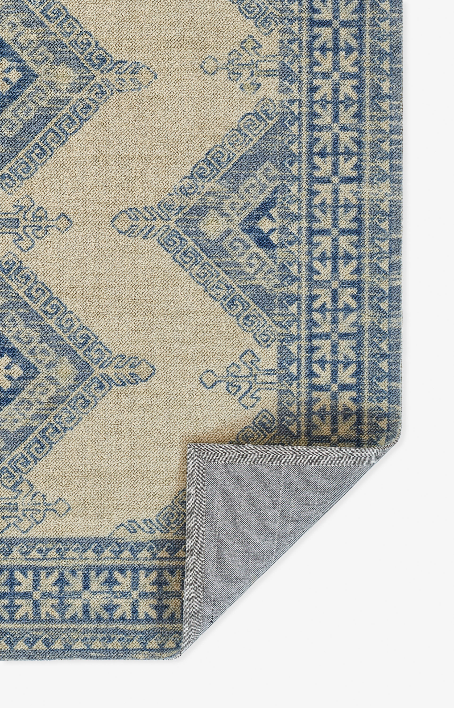 Beige woven area rug with blue geometric motifs and Greek-key border; corner folded to reveal backing.
