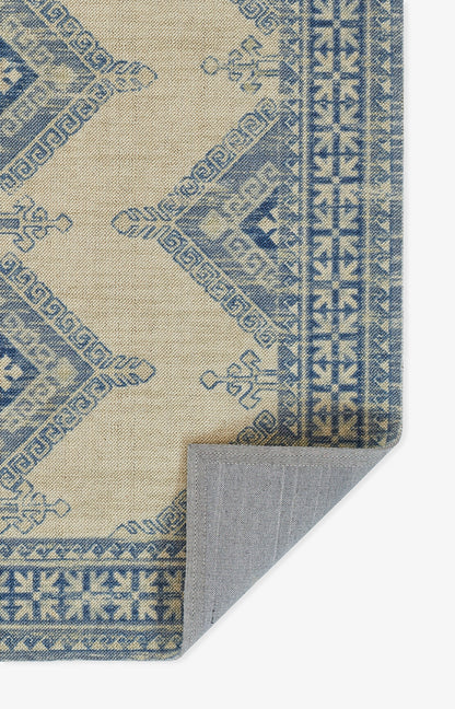 Anatolian-style ivory rug with indigo geometric motifs and a decorative border; folded corner shows the underside.