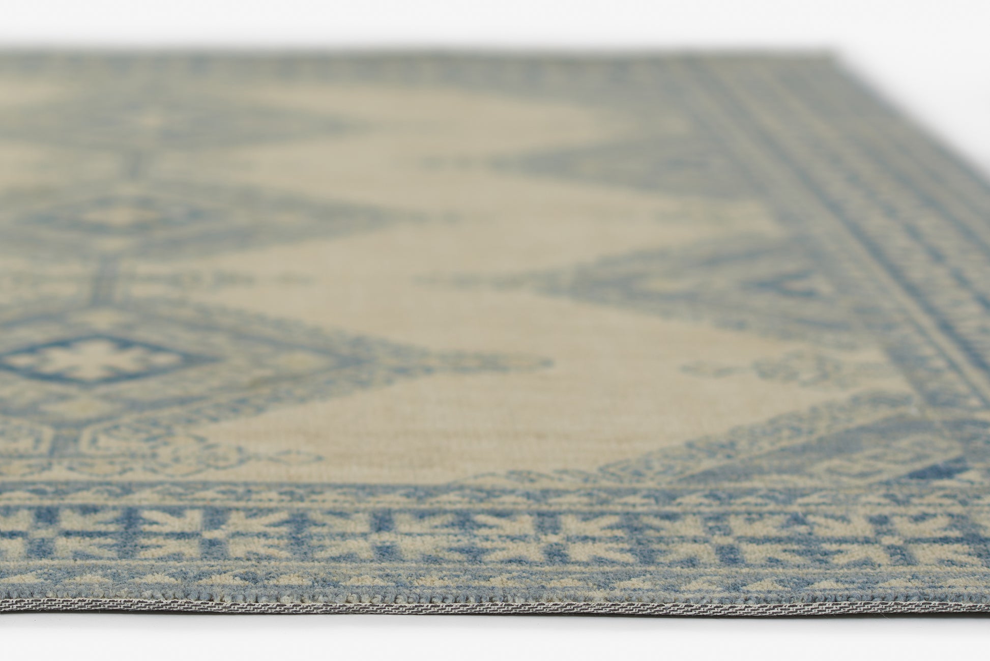 Woven rug in ivory & blue with an oriental geometric border; rectangular, close-up edge view.