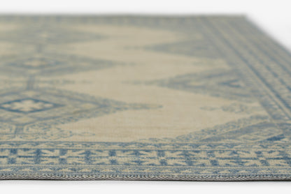 Woven rug in ivory & blue with an oriental geometric border; rectangular, close-up edge view.